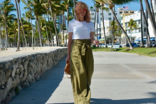 Mujer caminando por Ocean Drive en Miami Beach, con palmeras al fondo.