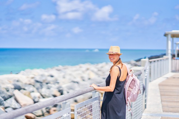 Mujer con vestido de verano y sombrero en un muelle de una playa rocosa en Miami.