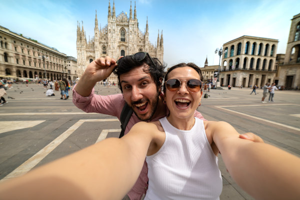 Pareja feliz tomándose una selfie frente a la Catedral del Duomo en Milán en un día soleado.
