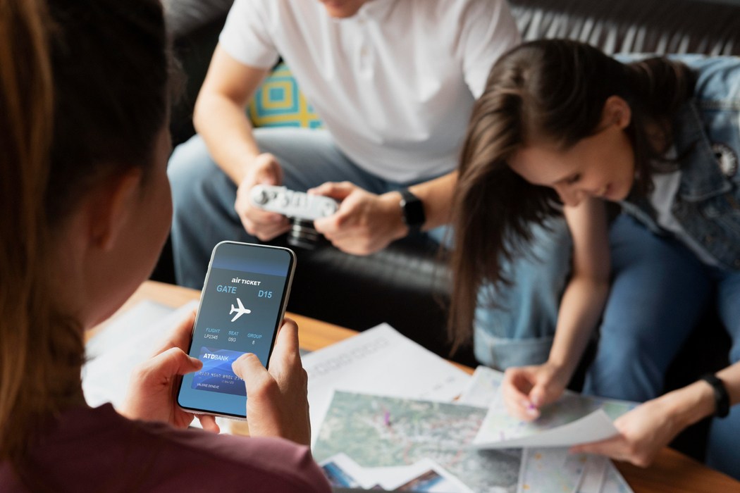 Pessoa segura celular com bilhete aéreo digital enquanto grupo planeja roteiro com mapas, ilustrando o que é milhas no contexto de viagem.