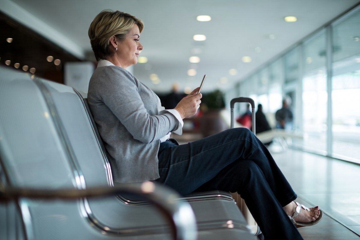 Mulher usa celular enquanto aguarda voo em aeroporto, simbolizando o conhecimento dos direitos previstos pela Convenção de Montreal.