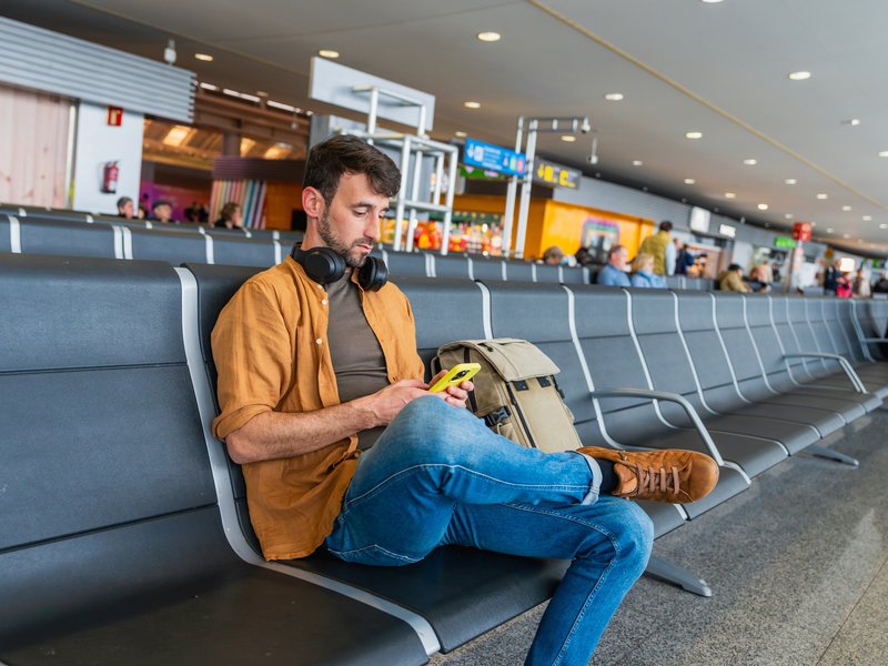 Viajante consultando informações de saúde em um smartphone enquanto aguarda em um aeroporto, conceito de prevenção e cuidados durante viagens internacionais.