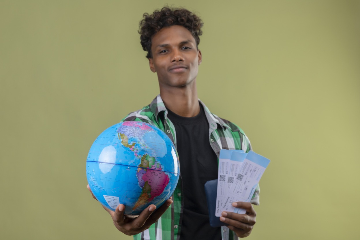 Jovem segurando um globo terrestre e passagens aéreas, simbolizando planejamento e escolha do melhor seguro viagem