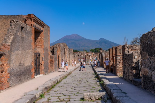 Personas turistas recorriendo las ruinas de Pompeya con el Vesubio en el fondo, una de las cosas que ver en Nápoles, Italia.