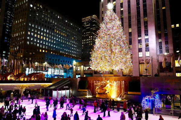 Árbol de Navidad del Rockefeller Center encendido por la noche con fuente de agua y pista de patinaje con gente debajo.
