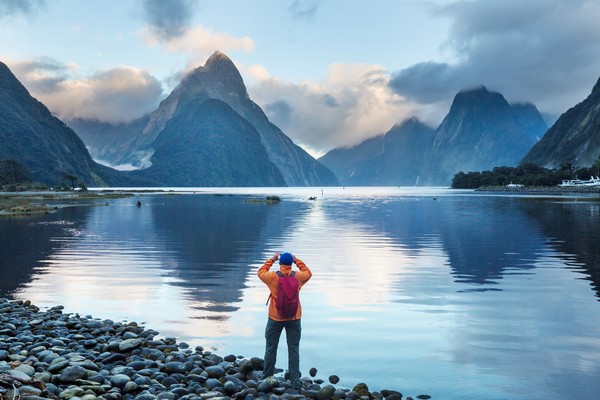 Viajero fotografiando el paisaje en Milford Sound, Nueva Zelanda, desde la orilla de un lago.