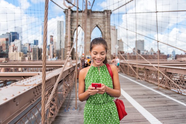 Mujer mirando su smartphone con una sonrisa en el puente de Brooklyn en la ciudad de Nueva York, Manhattan, EE.UU.