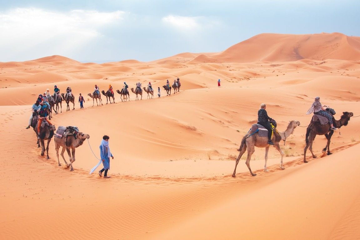 Foto de turistas fazendo passeio de camelo nas dunas de um deserto, ilustrando artigo sobre o que fazer em Marrocos.