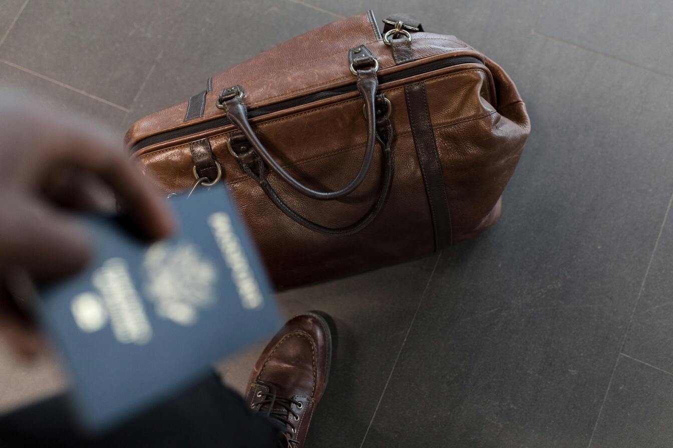 Imagem de uma mão de um homem segurando passaporte e uma mala no chão, em texto sobre o que pode levar na bagagem de mão em voo nacional