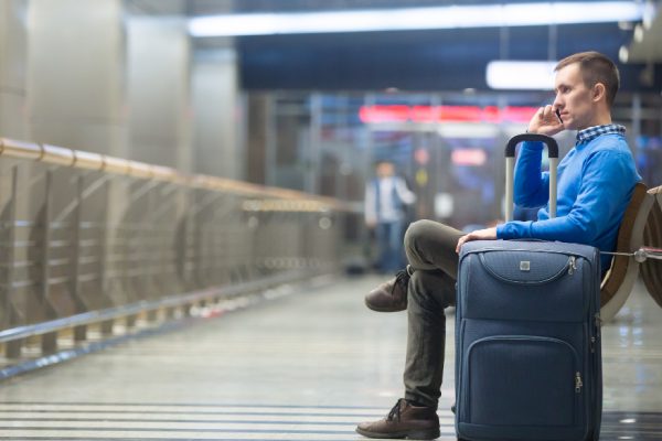 homem com bagagem em aeroporto e falando ao celular para aborar overbooking