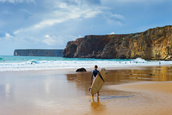 Mujer surfista con tabla de surf caminando por la orilla de una playa del Atlántico en Portugal, lista para ingresar al mar.
