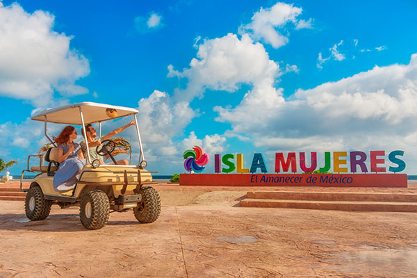 Pareja en vehículo junto a cartel de Isla Mujeres