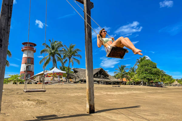 Mujer columpiándose en el balancín de Playa Venao frente al faro, Panamá, en un día soleado.