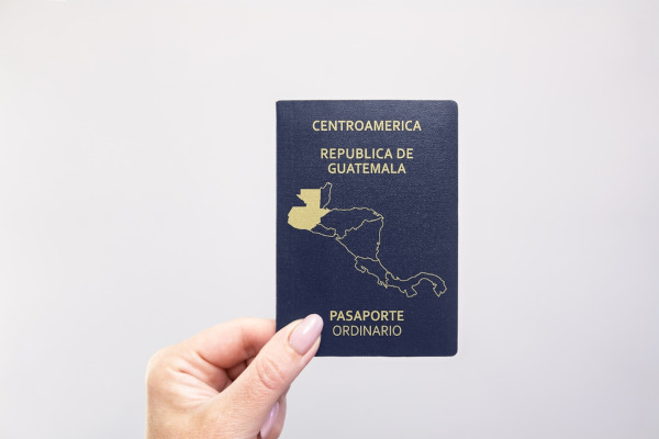 Persona mostrando pasaporte ordinario de la República de Guatemala sobre un fondo blanco liso.