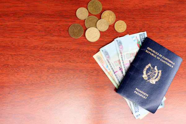 Monedas y billetes guatemaltecos junto con el pasaporte de Guatemala en una mesa de madera.