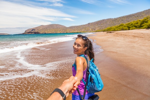 Mujer turista sonriente tomando de la mano a hombre en la playa de Espumilla, Isla de Santiago, Islas Galápagos, Ecuador.