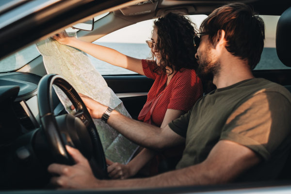 Hombre y mujer sentados en un coche, mirando un mapa y disfrutando de un viaje por carretera.