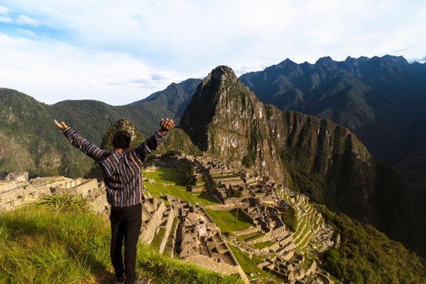 Turista con los brazos en alto contemplando la ciudadela de Machu Picchu.