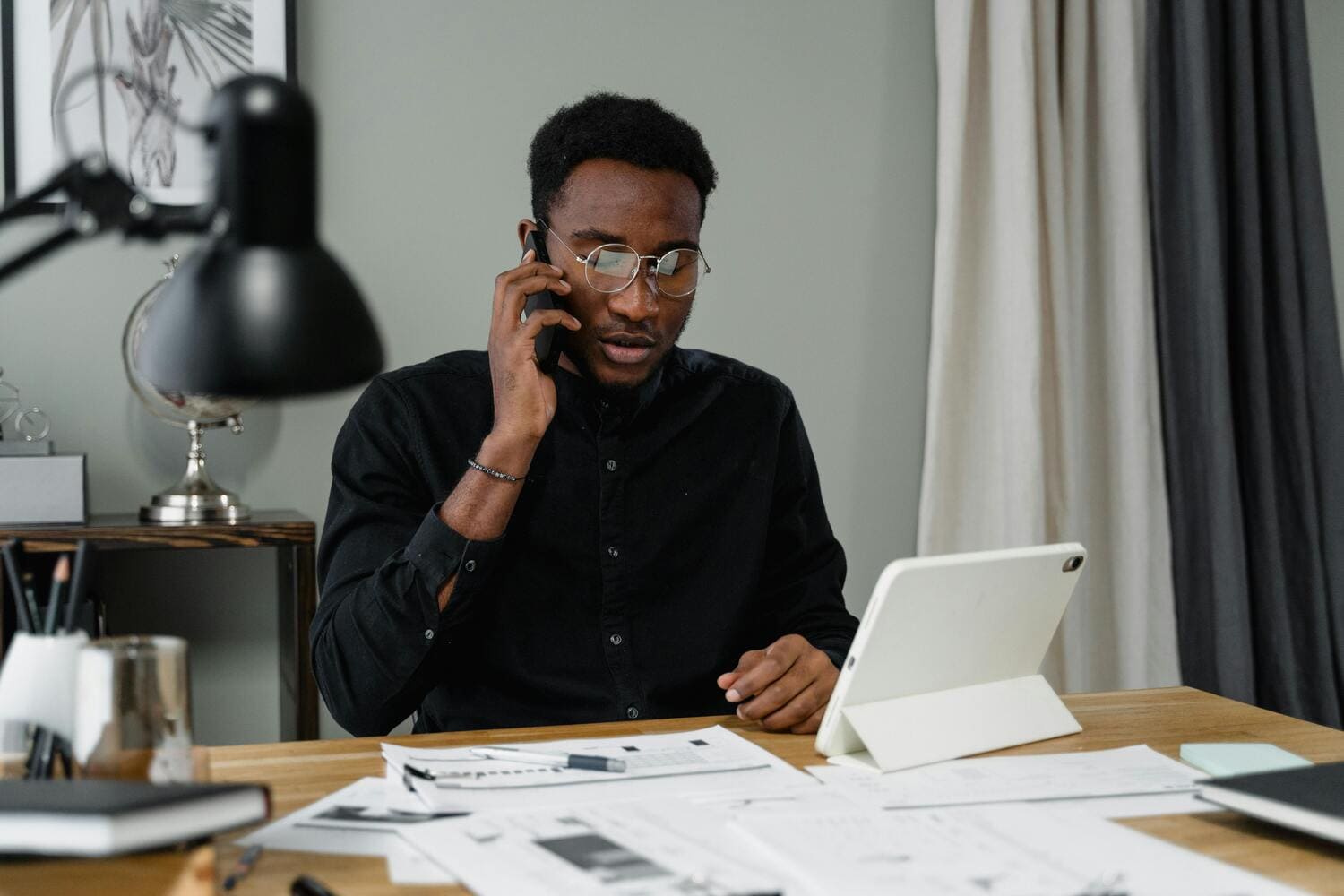 Pessoa fazendo anotações em uma mesa, em frente a um notebook, com um copo de café e um fone de ouvido ao seu lado