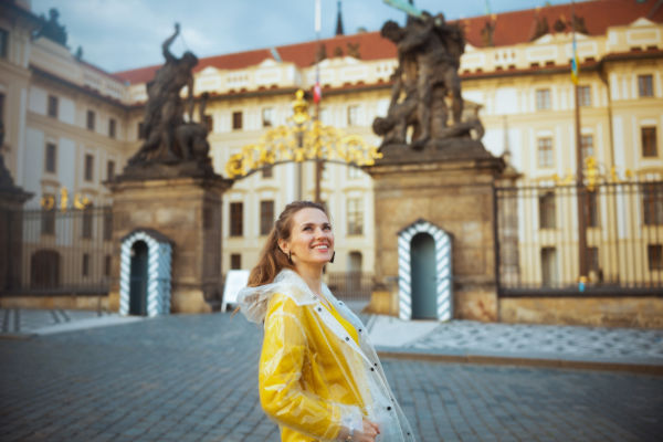 Turista con piloto amarillo sonríe frente a la entrada del Castillo de Praga, en República Checa.