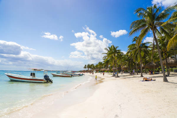 Praia tropical em Akumal, México, com areia branca, mar turquesa, palmeiras e barcos próximos à costa.