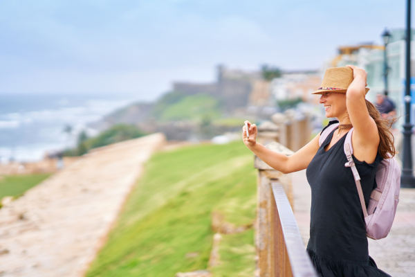 Mujer turista tomando fotos hacia la costa desde una barandilla en San Juan, Puerto Rico.