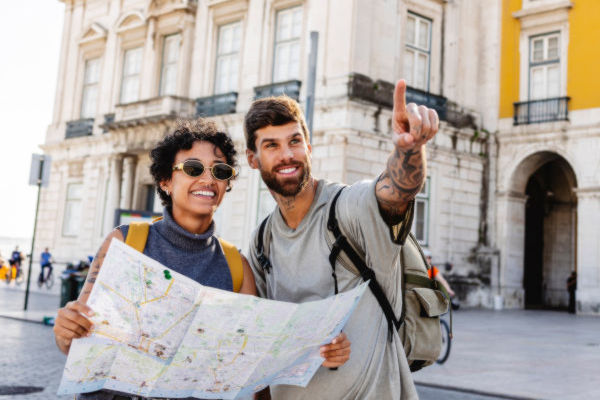 Pareja de viajeros con mochila consultando un mapa turístico en una plaza frente a un edificio histórico en Portugal.