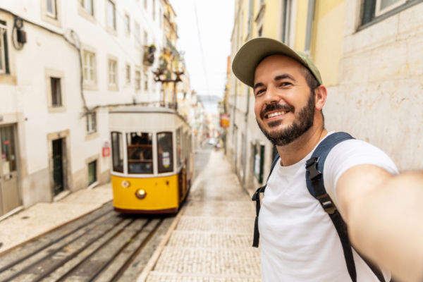 Turista tomándose una selfie frente al tradicional tranvía amarillo en una calle empedrada de Lisboa, Portugal.