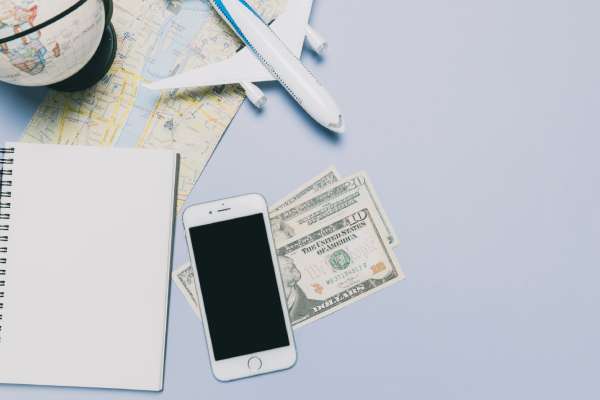 imagem de avião, celular, dinheiro e caderno na mesa para ilustrar o tema “quanto custa uma viagem para a itália