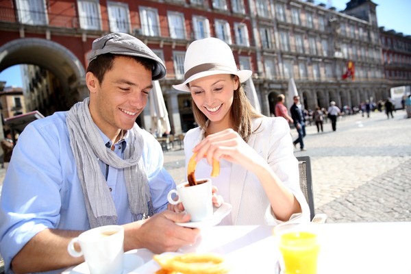Pareja sonriente comiendo churros con chocolate a la taza en Madrid.