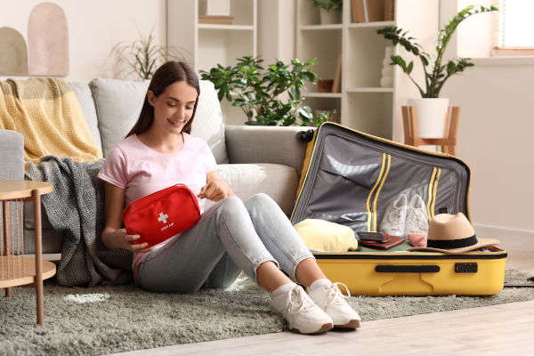 Mujer sentada en el suelo preparando un botiquín de primeros auxilios para colocarlo en una maleta abierta a su lado.