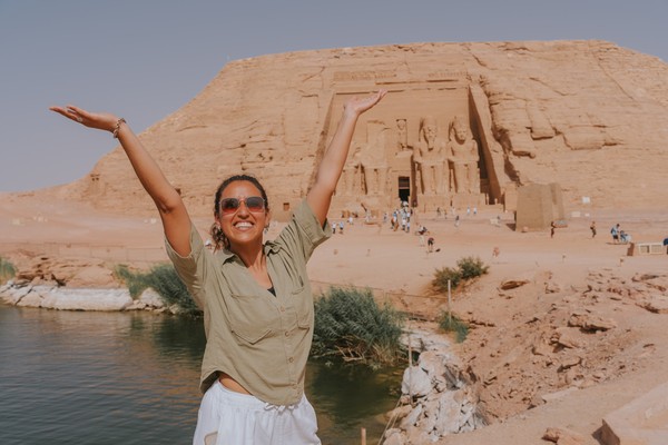 Mujer turista feliz levantando los brazos frente al gran templo de Abu Simbel, un sitio histórico en Egipto