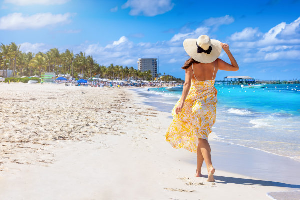 Mujer turista con sombrero y vestido floreado amarillo en una playa en Nassau, Bahamas