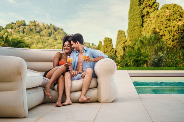 Pareja sentada en un sillón muy cómodo junto a una piscina con bebidas en un resort de lujo.