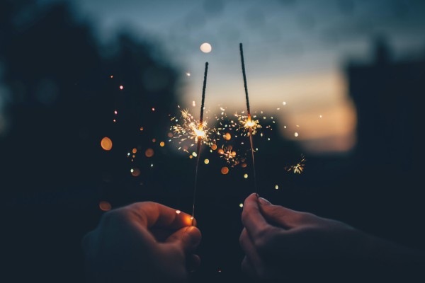 imagem de mãos segurando velas que soltam faíscas para ilustrar a virada de ano