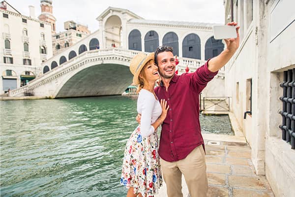 una pareja sonriente se saca una foto en un canal de Venecia