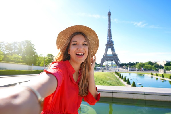 Mujer turista tomándose una selfie con la torre Eiffel de fondo en un día soleado en París, Francia
