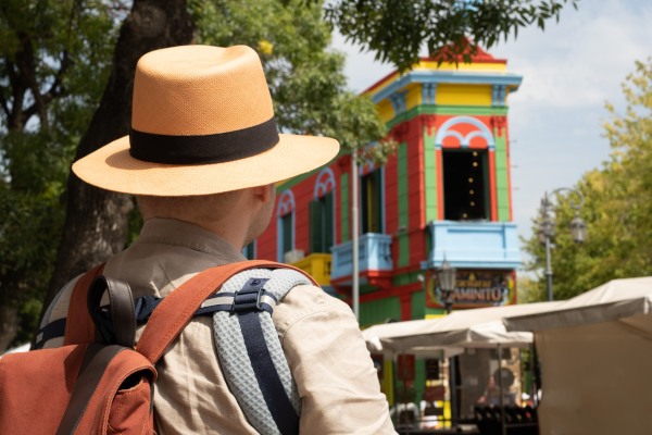 Vista trasera de un turista con sombrero y mochila mirando la entrada colorida de Caminito, en el barrio de la Boca, Buenos Aires, Argentina