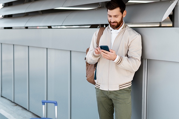 Homem mexendo com celular e com uma mala de viagem