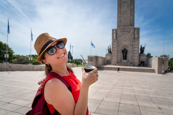 Mujer turista feliz tomando mate frente al monumento a la bandera en Rosario, Argentina.