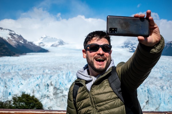 Hombre turista feliz tomándose una selfie junto al glaciar Perito Moreno en la Patagonia argentina.