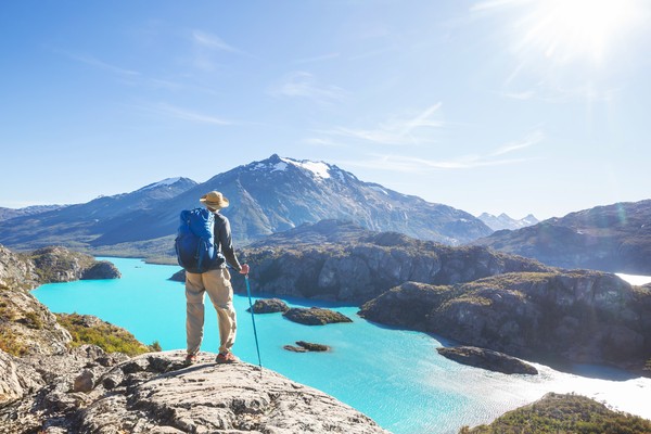 Hombre senderista en lo alto de una montaña patagónica con vistas a un lago celeste en Argentina.