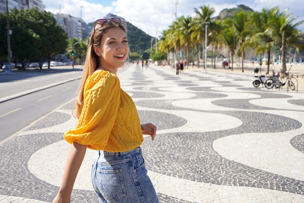 Mujer turista sonriente caminando por el paseo marítimo de la playa de Copacabana, Río de Janeiro.