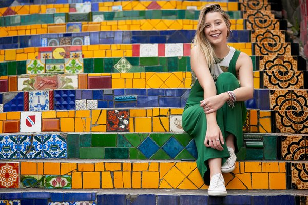 Mujer turista sonriente sentada en unos escalones de la Escalera Selarón con sus coloridos azulejos.