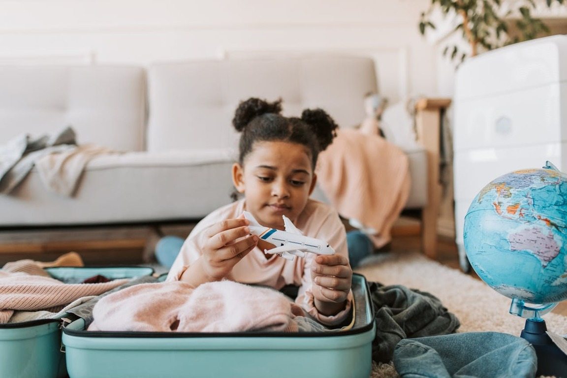 Menina brincando com avião de brinquedo enquanto arruma a mala, ilustrando artigo sobre quantos anos pode viajar sozinho de avião.