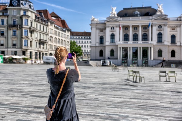 Mujer turista tomando fotografías con su smartphone de la Ópera de Zúrich en un día soleado en Suiza.