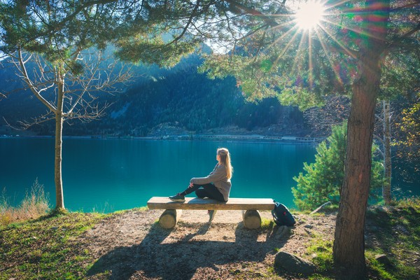 Mujer joven sentada en un banco de tronco frente a un lago alpino turquesa entre montañas en Suiza.