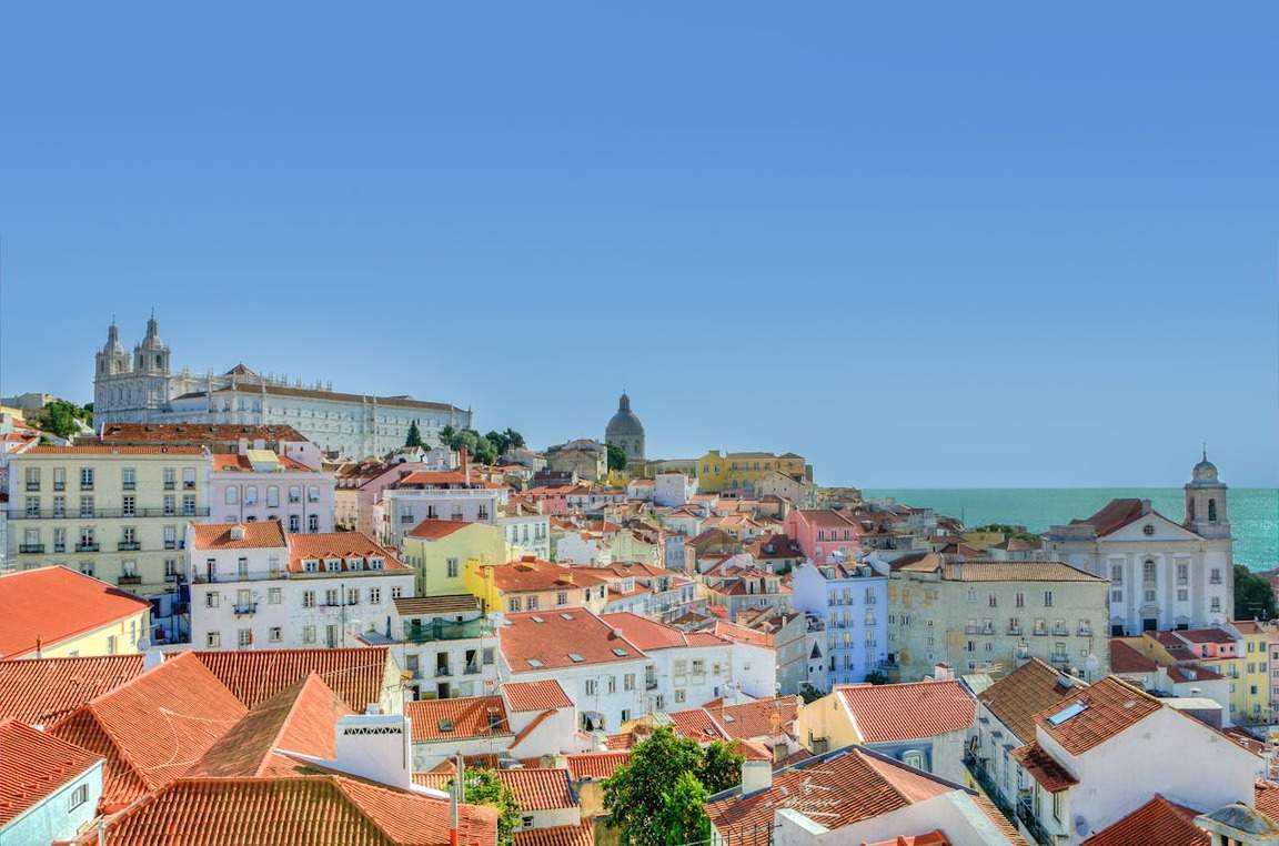 Imagem da vista aérea de Lisboa com casas coloridas de arquitetura típica e mar ao fundo ilustrando artigo sobre seguro viagem Portugal.