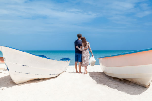 Pareja de turistas en la playa de Punta Cana observando el mar Caribe entre dos botes.
