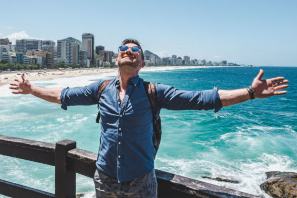 Turista disfrutando de la vista al mar en Río de Janeiro con los brazos abiertos, de pie frente a la playa de Ipanema.